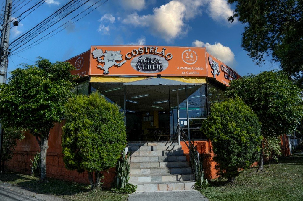 Fachada do Costelão Água Verde em Curitiba: letreiro na esquina, fachada laranja e salão com vidros — aberto 24 horas